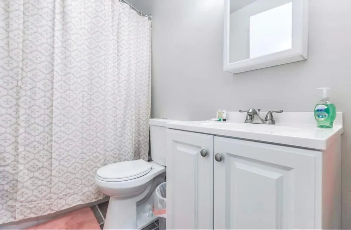 A bright and serene bathroom with a white vanity, large mirror, and a fresh shower curtain. The setup is ideal for personal grooming routines and offers a tranquil space for self-care, helping guests start or end their day refreshed.