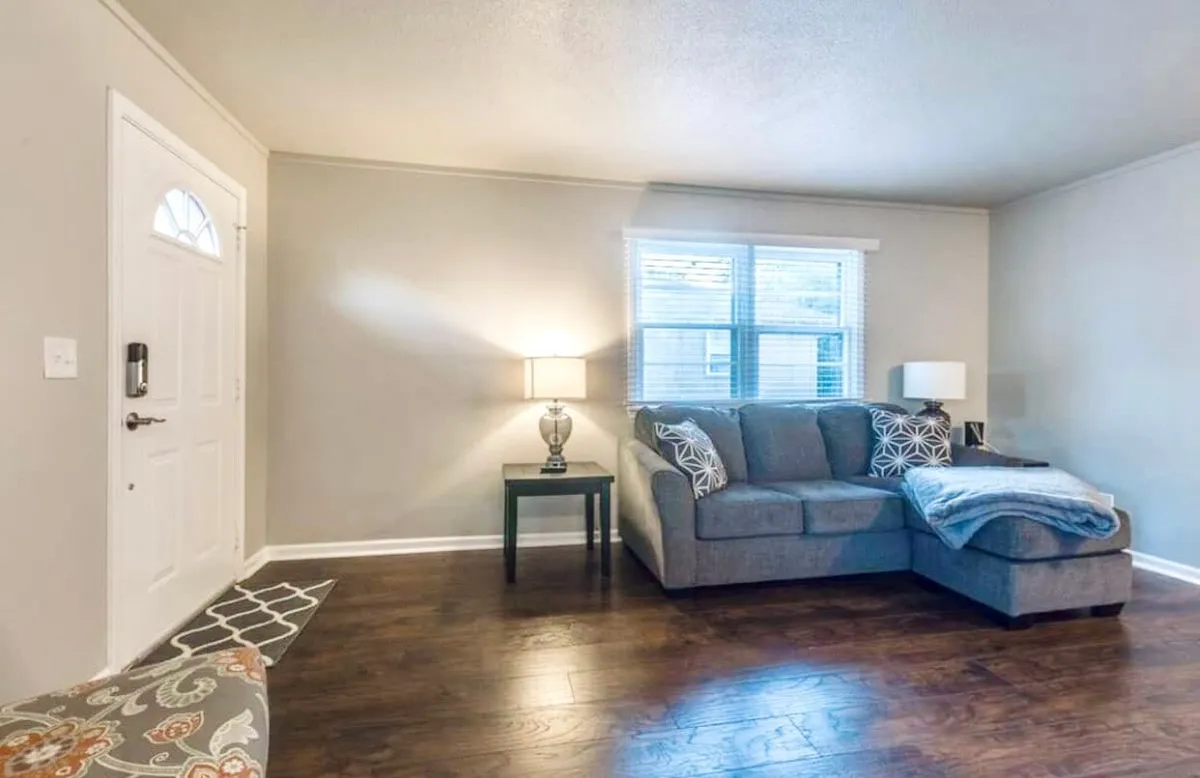 A cozy interior living space with a comfortable sofa, coffee table, and a stylish lamp beside a doorway. The scene exudes a sense of calm and comfort, ideal for both relaxation and focused work. Natural light filters in, creating a welcoming atmosphere conducive to productivity.