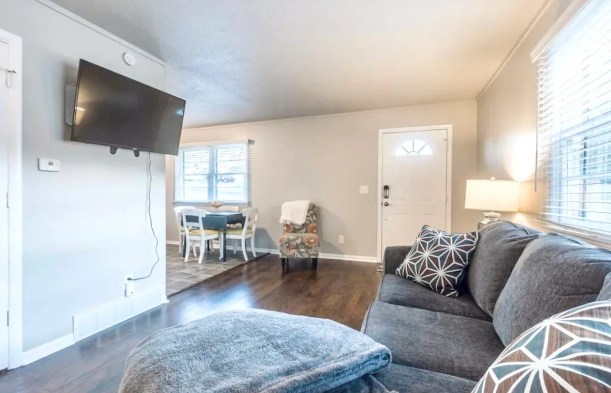 A welcoming interior scene featuring a plush sofa with decorative pillows, a dining table nearby, and the front door visible in the background. The arrangement suggests a space designed for comfort, conversation, and shared experiences, with warm lighting enhancing the cozy ambiance.