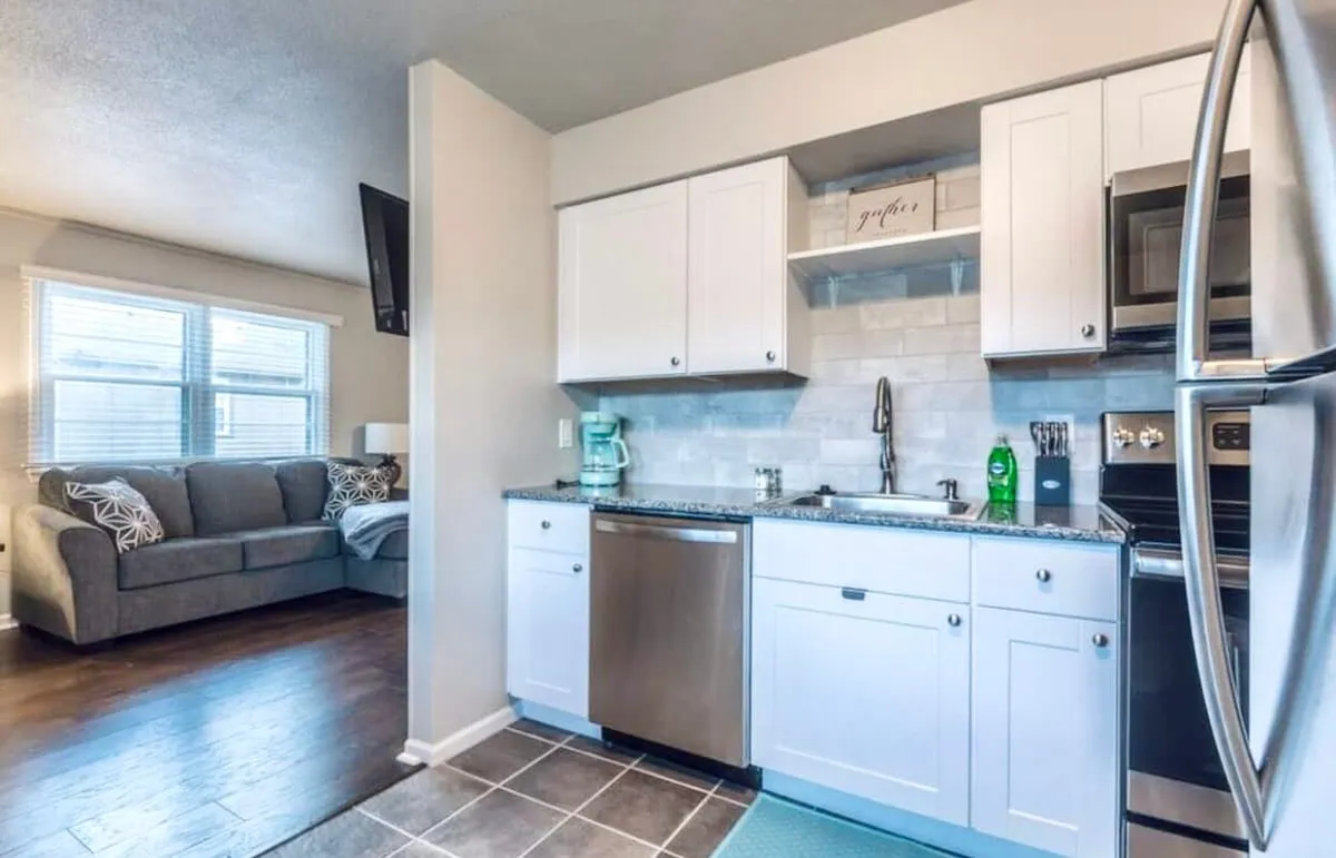 An inviting open-plan area featuring visible kitchen appliances, a well-organized countertop, and a nearby cozy couch. The space is designed for adaptability, with clear sightlines between dining, cooking, and relaxing areas. It offers ample table space for dining or setting up a laptop for work.